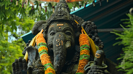 An old stone statue of Ganesha covered with moss with a wreath of yellow flowers on his neck...