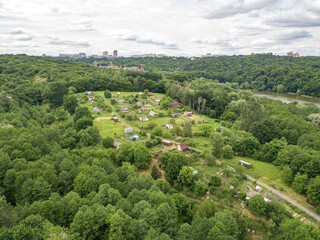 Fototapeta premium Low-rise settlement among green deciduous forest. Aerial drone view.