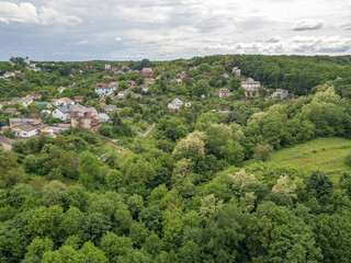 Fototapeta premium Low-rise settlement among green deciduous forest. Aerial drone view.
