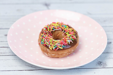 Pastries concept. Donuts with chocolate glaze with colorfull sprinkles, on a pink plate. Top view