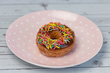 Pastries concept. Donuts with chocolate glaze with colorfull sprinkles, on a pink plate. Top view