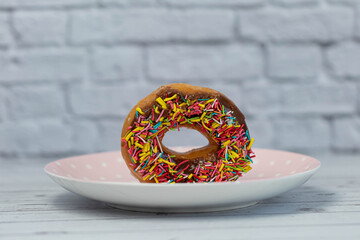 Pastries concept. Donuts with chocolate glaze with colorfull sprinkles, on a pink plate. side view