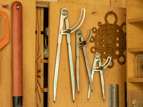 Carpentry workshop. Three iron compasses of different sizes hang on the door of a wooden box.