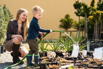 Female gardener and her son watering the plants in pots with a hose