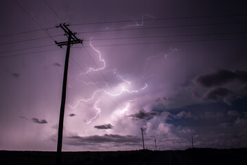 A powerful storm fills the night sky with lightning bolts, behind the silhouette of power lines.