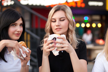 Pretty young women eating hamburger outdoor on the street