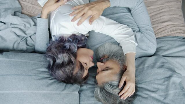 High angle view of happy couple man and woman in pajamas lying in bed hugging caressing each other expressing love and tenderness. Family and affection concept.