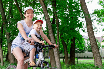 Naklejka na ściany i meble mother and son ride a Bicycle, mother carries a child in a child's chair on a Bicycle in the Park in the summer