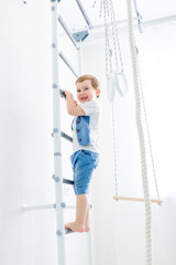 a child on the Swedish wall plays sports at home, a boy climbs a ladder with a rope, the concept of sports and health