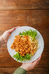 A plate of bolognese decorated with herbs in women's hands.
