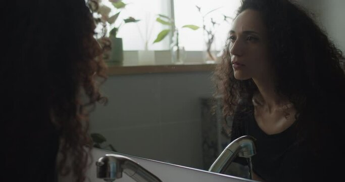 Close up of an insecure woman staring at herself while water running in the sink. Slow motion, handheld.