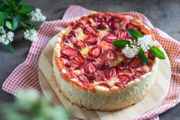 Baked strawberry pie cake tart with flowers on red napkin on rustic wooden table. Selective focus