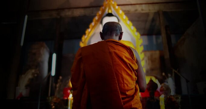 A back view slow motion of Buddhist monk kneels and pays homage to the Buddha three times in a very old church.