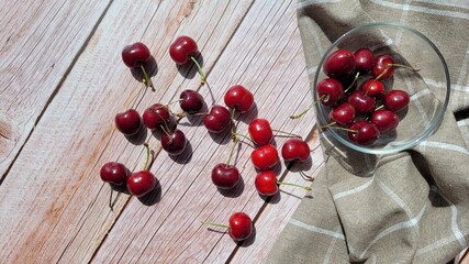 View on top of sweet red cherries in bowl and brown napkin on the side, selective focus, copy space. Sunlight coming over the table, shadows. Eating fruits outside in summer day. Raw images, unedited.