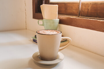 Hot latte coffee served in white mug on the table in warm morning.