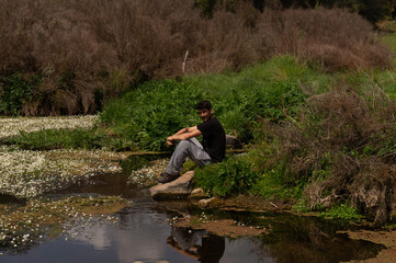 Fototapeta na wymiar person sitting on a rock in the river at spring