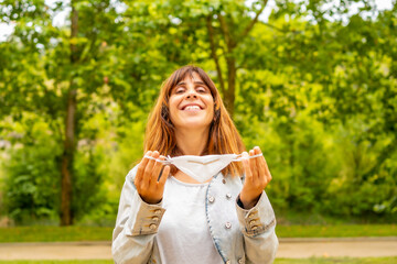 A young woman removing her surgical mask and smiling at the end of the coronavirus pandemic. End of restrictions abroad, happy to be able to breathe well again, covid19, yellow background