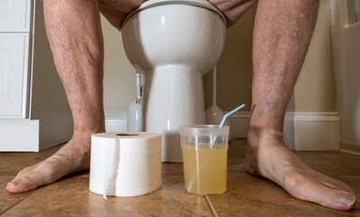Close up of legs of senior caucasian adult sitting on toilet preparing for colonoscopy with medication - Powered by Adobe