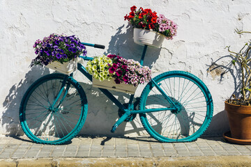 Bicycle with flower baskets leaning against an old white wall