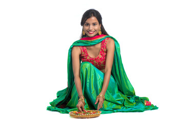 Portrait of a Indian Traditional Girl holding Diya and making Rangoli. Girl Celebrating Diwali or...