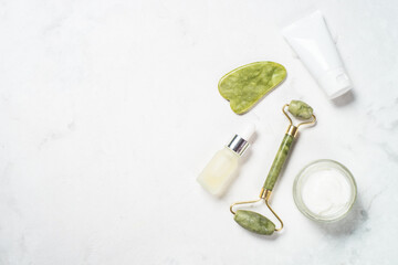 Face massagers and Scincare product. Jade roller, gua sha with face cream and serum bottle. Top view at white with copy space.
