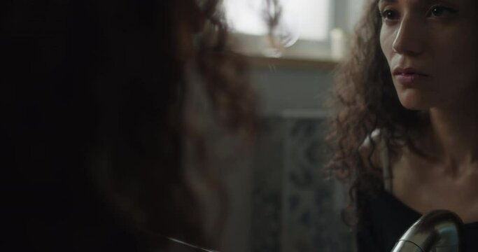 Close up of an insecure woman staring at her reflection in the mirror, feeling lonely and sad. Slow motion, handheld.