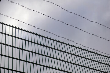 High fence with barbed wire against a dark sky with gray clouds.