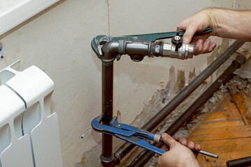 A plumber fitter fastens a tap to a pipe to connect a new heating radiator.