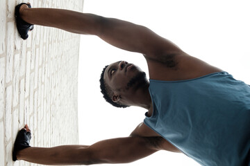 Fit young black man stretching against a brick wall.