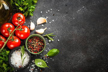 Food background at black table. Tomatoes, spices, herbs and olive oil. Ingredients for cooking. Top view with copy space.