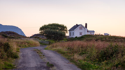 Rural white wooden vacation home or farm house with gravel path and hayfield in the evening