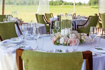 Flower arrangement on a set table. Summer tent with green chairs