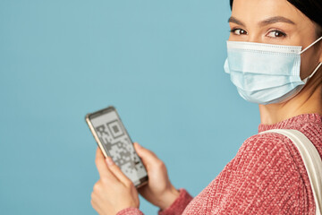 Pretty young lady using smartphone and wearing disposable medical mask