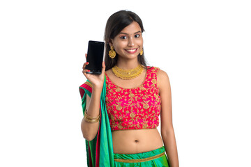 Young Indian traditional girl using a mobile phone or smartphone and showing blank screen smart phone on white background