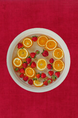 a red textured background with a large bowl of oranges and strawberries floating in water for a fruit bath