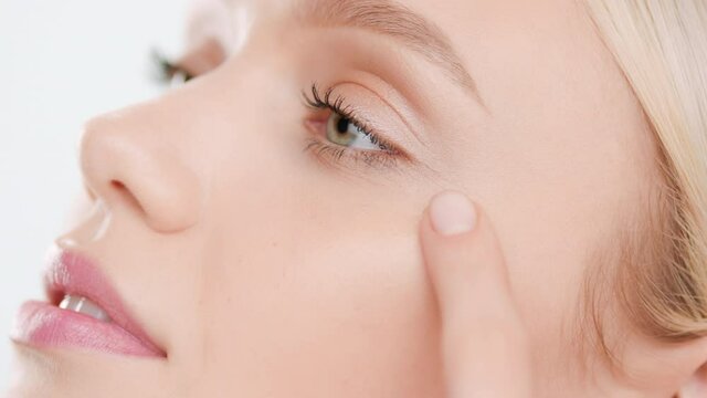 Big close-up shot of pretty fit European young woman with golden hair applies skin care serum on her cheek on white background | Skin care serum commercial