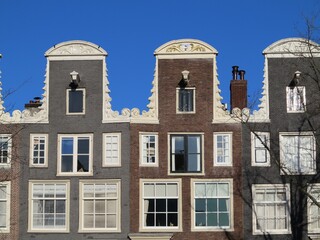 Fototapeta na wymiar Amsterdam Historic Canal House Facades with Neck Gables Close Up Against a Blue Sky