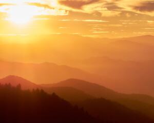 Sunset in the Smoky Mountains. The image is overly orange with a burst of sunshine in the upper left corner