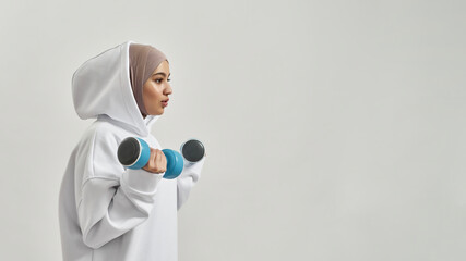 Attractive young arabian woman in hijab holding dumbbells