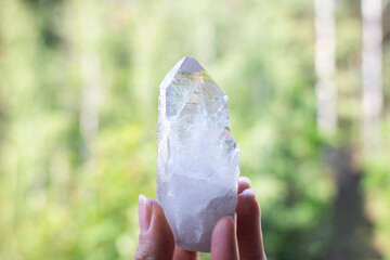 Hand holding a clear quartz crystal with green background.