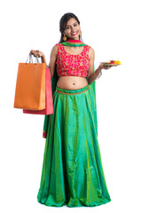 Beautiful Indian young girl holding and posing with shopping bags and pooja thali on a white...