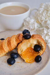 Hot crispy croissant with jam and blueberries with morning coffee on a light background. Aromatic pastries for breakfast. Lifestyle, modern trendy food concept