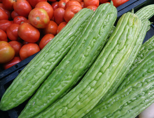 Pile of Vibrant Green Bitter Cucumber or Balsam Pear with Basket of Tomatoes in the Backdrop	