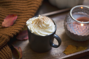 Cozy autumn cup of coffee with cream and cinnamon, blanket and candle