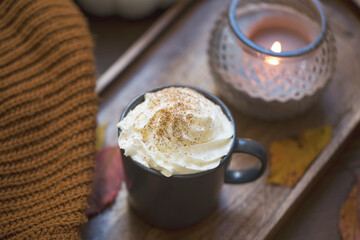 Cozy autumn cup of coffee with cream and cinnamon, blanket and candle
