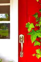 Closeup of bronze gold door handle on red door with ivy