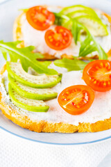Two toasts with avocado and arugula on a plate. Avocado toasts with cream cheese and cherry tomatoes. Diet food. Close-up