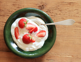 Delicious yogurt with strawberries in green bowl on wooden background, top view