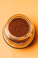 Medium-coarse ground coffee powder in glass cup on orange background