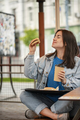 Obraz premium Street portrait of cheerful young woman eating fast food.